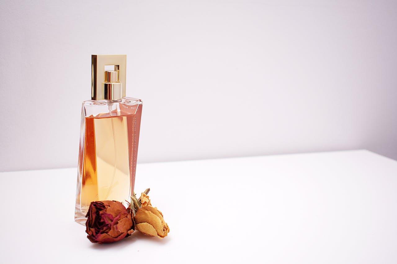about-us Elegant glass perfume bottle with luxurious design placed next to dried flowers against a minimalistic white background.
